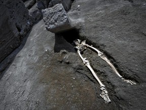 The legs of a skeleton emerge from the ground beneath a large rock believed to have crushed the victim's bust during the eruption of Mt. Vesuvius in A.D. 79, which destroyed the ancient town of Pompeii, at Pompeii's archeological site, near Naples, on Tuesday, May 29, 2018.