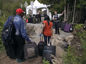 In this Aug. 7, 2017 file photo, a Royal Canadian Mounted Police officer informs a migrant couple of the location of a legal border station, shortly before they crossed from Champlain, N.Y., to Saint-Bernard-de-Lacolle, Quebec, using Roxham Road.