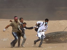 Palestinian protestors carry a wounded comrade during a protest near the border fence with Israel east of Jabalia in the central Gaza Strip on May 15, 2018.  Palestinians were gathering today for fresh protests along the Gaza border, a day after Israeli forces killed dozens there as the US embassy opened in Jerusalem on what was the conflict's bloodiest day in years.