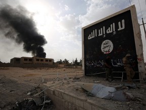 Iraqi fighters of the Hashed al-Shaabi (Popular Mobilisation units) stand next to a wall bearing the ISIL flag as they enter the city of al-Qaim, in Iraq's western Anbar province near the Syrian border, Nov. 3, 2017.