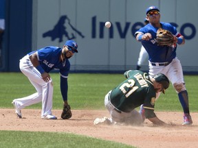 Toronto Blue Jays' Richard Urena and teammate Yangervis Solarte manage to force out Oakland Athletics' Jonathan Lucroy at second base during sixth inning American League MLB baseball action in Toronto on Sunday May 20, 2018.