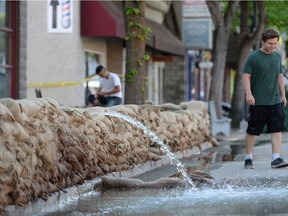 A man walks pass as water is pumped from a business in the downtown area in Grand Forks, in the Boundary Country of the West Kootenay region of British Columbia, on Tuesday, May 15, 2018.