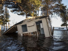 A cottage rests toppled in water after being battered by floodwater from the Saint John River on Grand Lake in New Brunswick on Friday, May 11, 2018.