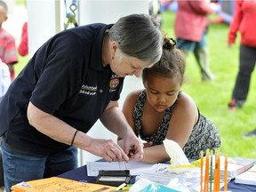 Samarah Adan gets a little help from an Ottawa Police volunteer when she puts her fingerprints in a book for the children's ID program, during Police Week events at Alexander Park on May 16.