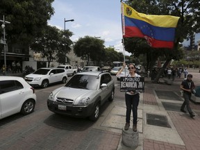 A demonstrator holds a Venezuelan national flag and a placard with a message that reads in Spanish: "Maduro, resign right now!" during a protest in Caracas, Venezuela, Wednesday, May 23, 2018. A small group protested the outcome of the May 20th presidential election. The election gives Maduro a second six-year term amid the oil-rich country's deepening economic crisis that has many Venezuelans struggling to afford food and medicine.