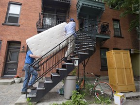 Jim and Eric Hendry carry a mattress up a staircase on what has become known as "Moving Day," in Montreal, Monday, July 1, 2013.