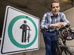 Ottawa City Councillor, Mathieu Fleury poses beside a sign asking cyclists to walk their bikes through a pedestrian tunnel under Nicholas St by the University of Ottawa campus.