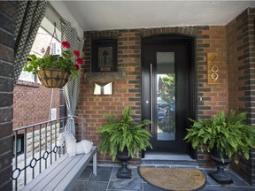 The owners of this Toronto home have decorated their front porch to match their own personal style. This includes hanging flower baskets, a black painted front door with matching windows, a custom number sign, and outdoor curtains.