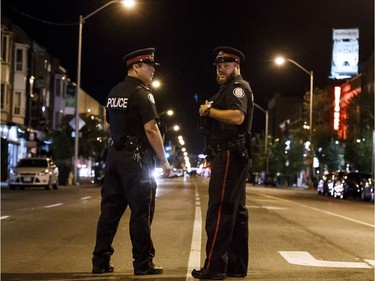 Toronto Police Officers stand watch at the foot of Danforth St. at the scene of a shooting in Toronto, Ontario, Canada on July 23, 2018.  A gunman opened fire in central Toronto on Sunday night, injuring 13 people including a child. Two dead incluiding gunman, police reported.