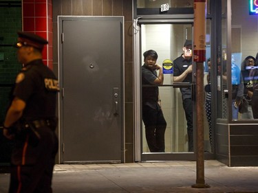People look out the window from a restaurant as Toronto Police afficers stand watch at Danforth St. at the scene of a shooting in Toronto, Ontario, Canada on July 23, 2018.  A gunman opened fire in central Toronto on Sunday night, injuring 13 people including a child. Two dead including gunman, police reported.