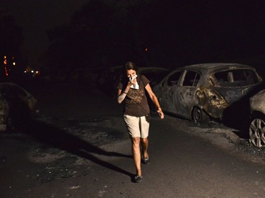 TOPSHOT - A woman walks in front of burnt cars at the village of Mati during a wildfire near Athens, on July 23, 2018. At least five people have died and more than 20 have been injured as wild fires tore through woodland and villages around Athens on Monday, while blazes caused widespread damage in Sweden and other northern European nations. More than 300 firefighters, five aircraft and two helicopters have been mobilised to tackle the "extremely difficult" situation due to strong gusts of wind, Athens fire chief Achille Tzouvaras said.