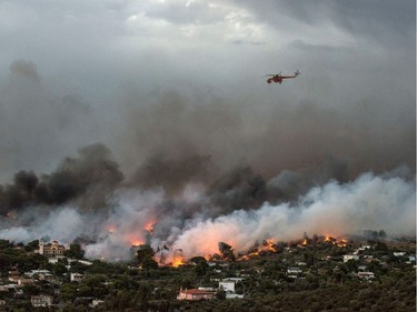 A firefighting helicopter flies over a wildfire raging in the town of Rafina near Athens, on July 23, 2018.  At least five people have died and more than 20 have been injured as wild fires tore through woodland and villages around Athens on Monday, while blazes caused widespread damage in Sweden and other northern European nations. More than 300 firefighters, five aircraft and two helicopters have been mobilised to tackle the "extremely difficult" situation due to strong gusts of wind, Athens fire chief Achille Tzouvaras said.
