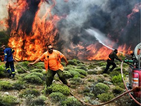 Firefighters and volunteers try to extinguish flames during a wildfire at the village of Kineta, near Athens, on July 24, 2018.  Raging wildfires killed 74 people including small children in Greece, devouring homes and forests as terrified residents fled to the sea to escape the flames, authorities said Tuesday.