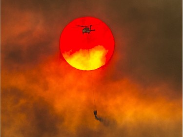 In this Friday, July 27, 2018 photo, a firefighting helicopter makes a water drop as the sun sets over a ridge burning near Redding, Calif., in efforts against the Carr Fire. Scorching heat, winds and dry conditions complicated firefighting efforts. (Hector Amezcua/The Sacramento Bee via AP) ORG XMIT: CASAB602