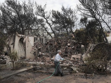 A woman sprays water outside her house that was damaged in the wildfires near the village of Neos Voutzas near Athens, Tuesday, July 24, 2018. Greece sought international help through the European Union as fires on either side of Athens left lines of cars torched, charred farms and forests, and sent hundreds of people racing to beaches to be evacuated by navy vessels, yachts and fishing boats.(AP Photo/Yorgos Karahalis) ORG XMIT: TH136
