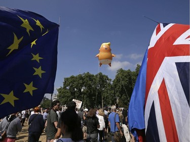 An EU, left, and a British union flag are displayed in front of a six-meter high cartoon baby blimp of U.S. President Donald Trump, as it is flown as a protest against his visit, in Parliament Square in London, England, Friday, July 13, 2018.