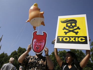 Protestors hold up banners as a six-meter high cartoon baby blimp of U.S. President Donald Trump, as it is flown as a protest against his visit, in Parliament Square in London, England, Friday, July 13, 2018.