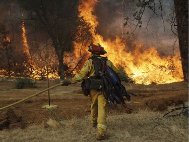 A firefighter walks to flames as a wildfire advances onto a residential district Saturday, July 28, 2018, in Redding, Calif.
