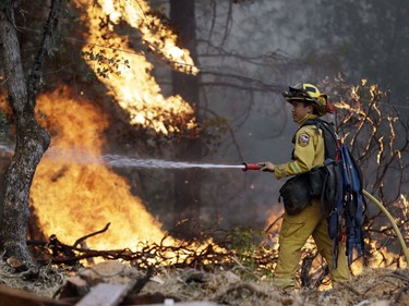 A firefighter hoses down flames as a wildfire advances onto a residential district Saturday, July 28, 2018, in Redding, Calif.