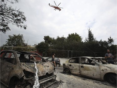 A firefighting helicopter flies above burned-out cars in Mati east of Athens, Tuesday, July 24, 2018. Twin wildfires raging through popular seaside areas near the Greek capital have torched homes, cars and forests and killed at least 49 people, authorities said Tuesday, raising the death toll after rescue crews reported finding the bodies of more than 20 people huddled together near a beach.