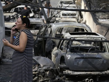 A woman reacts as she stands amid the charred remains of burned-out cars in Mati east of Athens, Tuesday, July 24, 2018. Twin wildfires raging through popular seaside areas near the Greek capital have torched homes, cars and forests and killed at least 49 people, authorities said Tuesday, raising the death toll after rescue crews reported finding the bodies of more than 20 people huddled together near a beach.