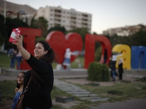 FILE - In this Wednesday, July 18, 2018 file photo, a Syrian woman uses her mobile phone to take a family selfie with artwork behind declaring "I Love Damascus" at Omayyid Square, in Damascus, Syria. The celebratory mood in government-controlled areas stems from successive military advances in the past year and an impression that President Bashar Assad, with massive support by unwavering allies Russia and Iran, has won the war or at least militarily defeated the opposition trying to topple him.