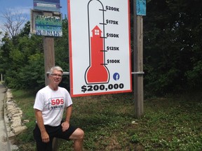 Bruce McConville poses beside the SOS Vanier fund-raising sign on Saturday, July 28, 2018. The sign is part of a campaign to raise $200,000 for SOS Vanier's legal defence fund.