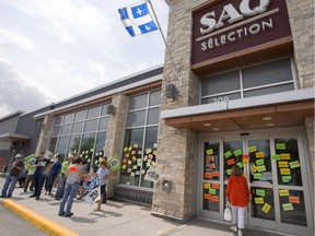 A customer looks through the windows as liquor store employees walk the picket line in front of an SAQ outlet on the first day of their strike to press lagging contract negotiations, Tuesday, July 17, 2018 in Rosemere, Que.