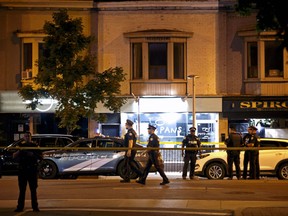 Toronto Police officers walk the scene at Danforth St. at the scene of a shooting in Toronto, Ontario, Canada on July 23, 2018. A gunman opened fire in central Toronto on Sunday night, injuring 13 people including a child. Police have reported that two are dead including gunman.