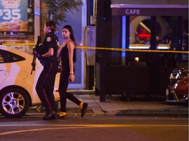 A police officer escorts a civilian away from the scene of a mass casualty event in Toronto on Sunday, July 22, 2018.