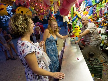 Natalie Cox, (L) looks on as her friend Avery Altose is given a prize by Yves Martineau after breaking a couple balloons while attending the RBC Bluesfest on the grounds of the Canadian War Museum at Lebreton Flats.