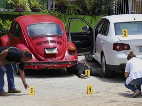 FILE - In this July 22, 2018 file photo, forensics place numbers by evidence near the body of a woman who was found dead between two cars parked outside a restaurant in Acapulco, Mexico. The number of homicides in Mexico in 2017 was higher than originally thought, according to the National statistics institute INEGI, which reports there were 31,174 slayings, not 29,168 reported by the Interior Ministry. INEGI says the homicide rate in 2017 broke down to 25 per 100,000 inhabitants.