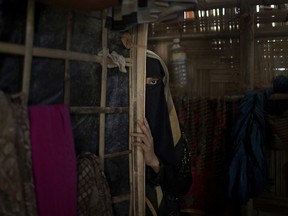In this Tuesday, June 26, 2018, photo, "A," a 13-year old Rohingya Muslim girl who agreed to be identified by her first initial, peers from behind a partition in her family's shelter in Jamtoli refugee camp in Bangladesh. Two months earlier, soldiers had broken into her home back in Myanmar and raped her, an attack that drove her and her terrified family over the border to Bangladesh. Ever since, she had waited for her period to arrive. Gradually, she came to realize that it would not. The pregnancy was a prison she was desperate to escape. The rape itself had destroyed her innocence. But carrying the baby of a Buddhist soldier could destroy her life.