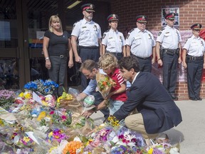 Prime Minister Justin Trudeau, accompanied by his four-year-old son Hadrien and Fredericton MP Matt DeCourcey, left, places flowers outside the police station in Fredericton on Sunday, Aug. 12, 2018.