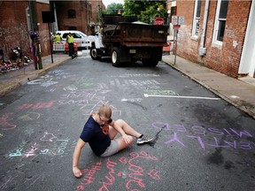 Kim Ganczak writes on the street with chalk near a makeshift memorial for Heather Heyer, who was killed one year ago Sunday during a deadly clash in Charlottesville, Va.