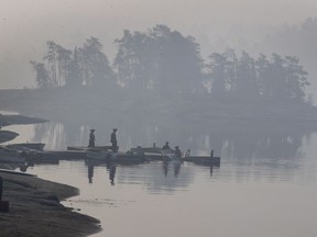 Smoke blankets the area as Ministry of Natural Resources firefighters work a boat at Flat Rapids Camp and Resort on the French River near Killarney, Ont., on Tuesday, July 31, 2018. The area is under forced evacuation orders due to forest fires burning nearby.