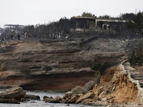In this file photo dated Tuesday, July 24, 2018, firefighters stand on the cliff top where burned trees hug the coastline in Mati east of Athens, after wildfires raged through the popular seaside areas near the Greek capital. The prime minister of Greece Alexis Tsipras pledged Thursday Aug. 9, 2018, to overhaul the national disaster response agency, as authorities publicly named all the people killed by the country's deadliest forest fire in decades.