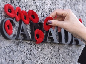 People place poppies over lettering in the National War Memorial during the National Remembrance Day ceremony in Ottawa on November 11, 2016.