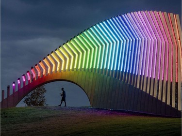 A man walks under Moving Surfaces, a giant steel and light sculpture at Ottawa's Lansdowne Park, as it is lit up in the colours of the rainbow, during Pride Week on Saturday, Aug. 25, 2018.