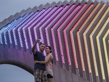 Taras Klymyshyn and Chantale Trottier take a photo of themselves in front of Moving Surfaces, a giant steel and light sculpture at Ottawa's Lansdowne Park, as it is lit up in the colours of the rainbow during Pride Week on Saturday, Aug. 25, 2018.