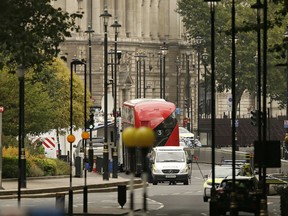 A forensics officer works near the scene near of a car that crashed into security barriers outside the Houses of Parliament to the right of a bus in London, Tuesday, Aug. 14, 2018. Authorities said in a statement Tuesday that a man in his 20s was arrested on suspicion of terrorist offenses after a silver Ford Fiesta collided with a number of cyclists and pedestrians before crashing into the barriers during the morning rush hour.