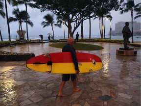 A surfer walks along Waikiki Beach in Honolulu during a light rain from Tropical Storm Lane on Saturday.