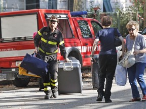 A firefighter pulls a suitcase and carries bags as he accompanies residents to get their belongings from their homes, in Genoa, Italy, Thursday Aug. 16, 2018. Authorities worried about the stability of remaining large sections of a partially collapsed bridge evacuated about 630 people from nearby apartments, some practically in the shadow of the elevated highway.