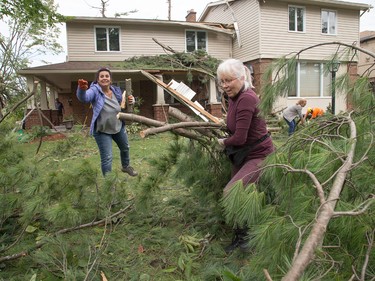Volunteers, including Sandra Monsour (l) and Karen Milner (R), came to help clear brush, branches and logs from Tracey Graham's home on Parkland Cres on Sunday morning as residents in Ottawa's Arlington Woods neighbourhood deal with the aftermath of the twister.