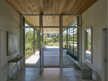 A view of the Rideau River is seen through the huge glass door at the front of the home. Rich oak wood extends from the ceiling of the front porch into the entrance of the house.