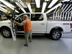 FILE- In this March 13, 2015, file photo, a worker inspects a new 2015 aluminum-alloy body Ford F-150 truck at the company's Kansas City Assembly Plant in Claycomo, Mo. Under pressure from U.S. safety regulators, Ford is recalling about 2 million F-150 pickups in North America because the seat belts can cause fires. The recall covers certain trucks from the 2015 through 2018 model years.