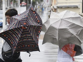 People walk in a strong wind as a typhoon approaches in Naha, Okinawa prefecture, southern Japan Saturday, Sept. 29, 2018.