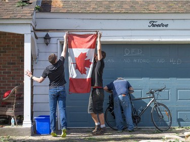 Jon Enos (R) and Zach Edwards (L) hang a Canadian flag they retrieved from the Arlington Woods home they were helping to clear of downed trees from on Saturday morning as residents in Ottawa's west end deal with the aftermath of the twister that touched down on Friday afternoon.
