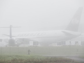 A man walks past an idle cargo jet as fog rolls over the Ottawa International Airport Thursday afternoon.