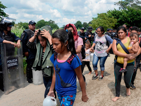 Migrants walk next to Mexican police officers after they swam across the Suchiate River from Ciudad Tecun Uman in Guatemala to Ciudad Hidalgo in Mexico, after a security fence on the international bridge was reinforced to prevent them from passing through, on Oct. 29, 2018.